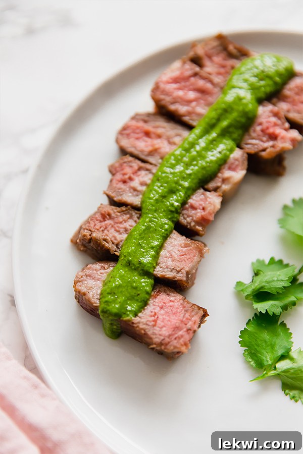 A white plate with steak topped with green sauce.