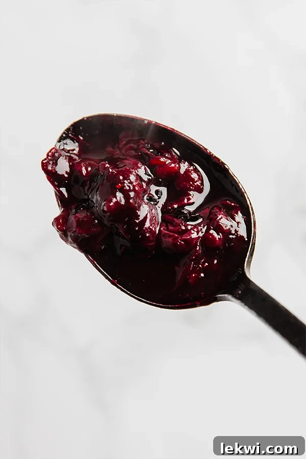 A small saucepan filled with vibrant blueberry balsamic sauce simmering on a stovetop, showing the softened blueberries.