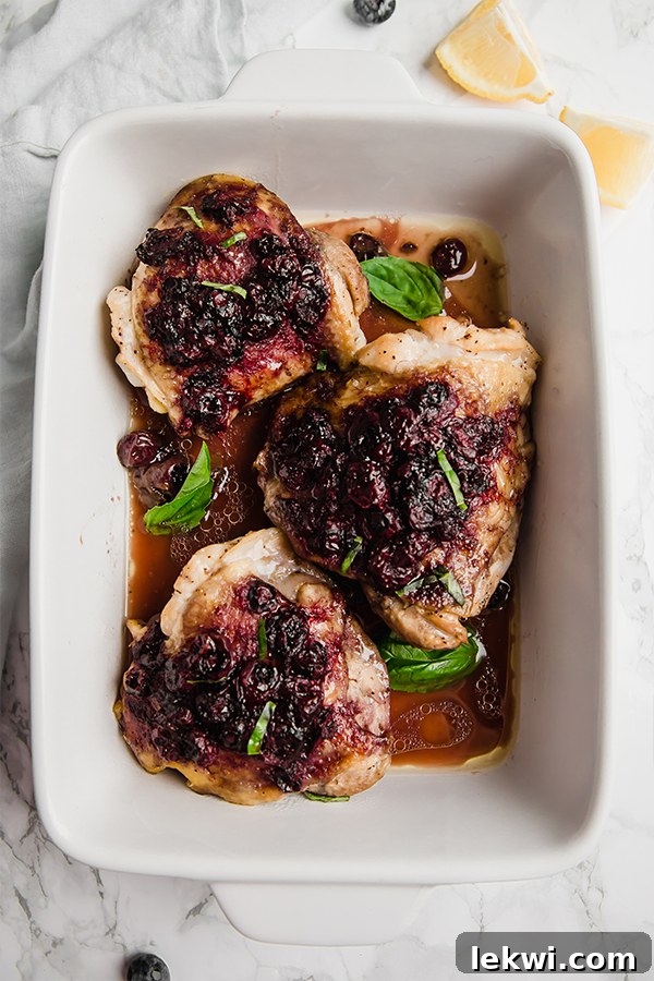 Chicken thighs baked in a white baking dish with blueberry balsamic sauce.