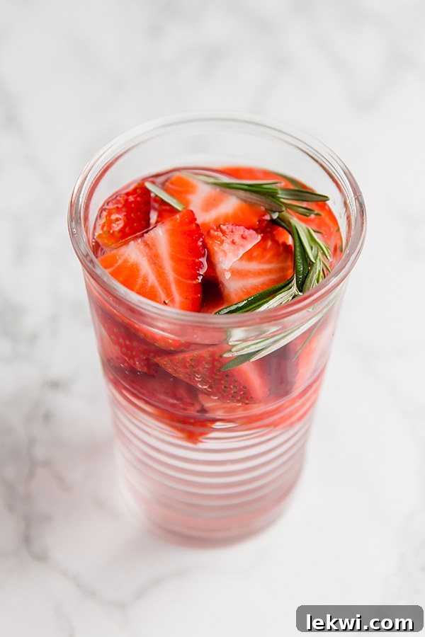 A drinking glass filled with water infused with strawberries and herbs.