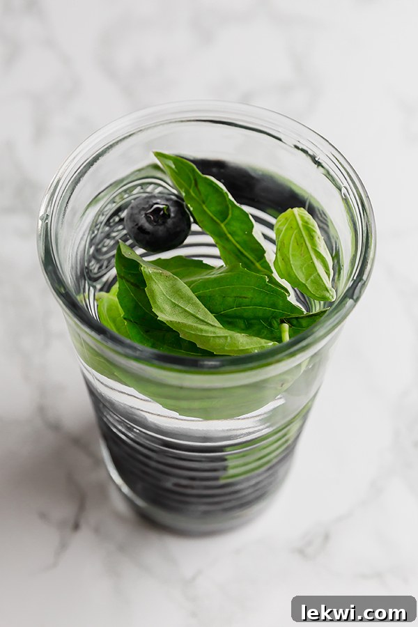 A drinking glass filled with water infused with blueberries and herbs.