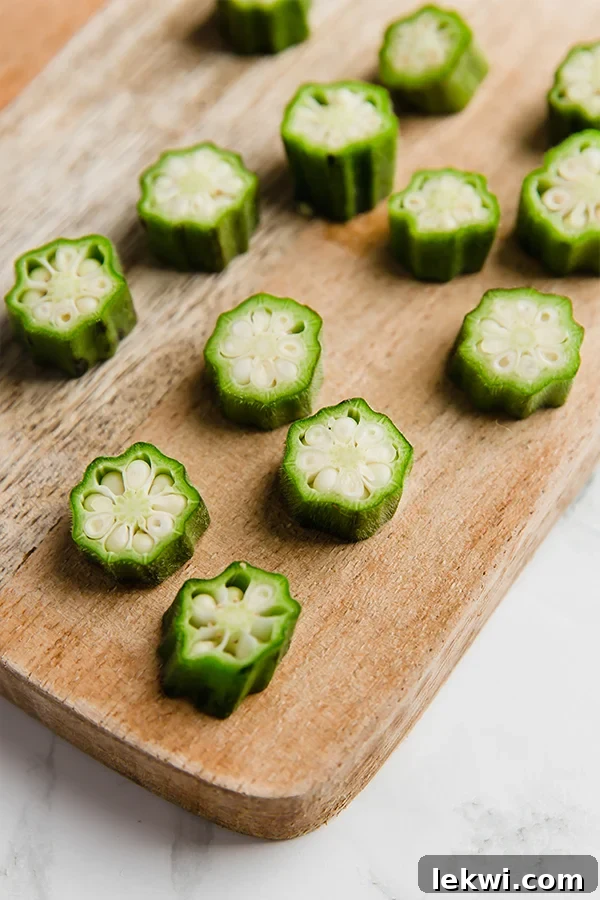 Fresh okra slices neatly arranged on a wooden cutting board, ready for roasting.