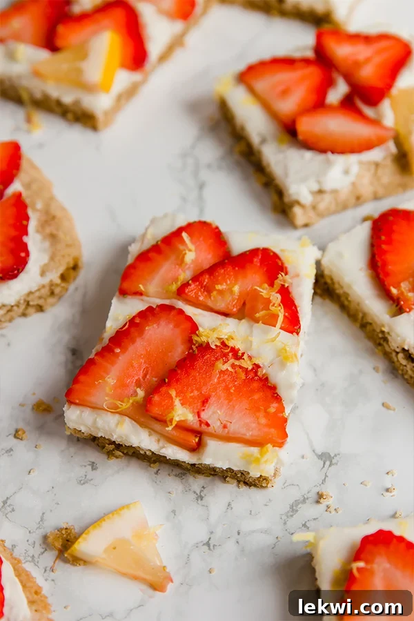 Lush strawberry lemon sugar cookie bars, topped with fresh slices of strawberry and bright lemon zest, neatly arranged on a rustic wooden board, ready to be enjoyed as a refreshing summer dessert.