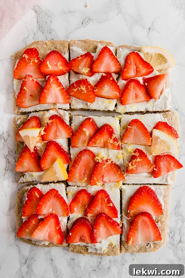 A close-up shot of a single strawberry lemon sugar cookie bar, showcasing its soft cookie base, creamy white frosting, fresh strawberry slices, and delicate lemon zest, inviting a delicious bite.