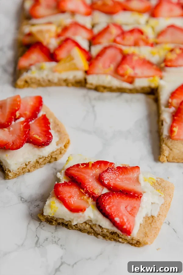 Several strawberry lemon sugar cookie bars, adorned with fresh strawberry slices and lemon zest, are displayed on a white serving platter, ready to be enjoyed as a refreshing treat.