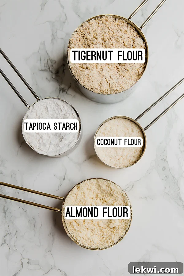 Measuring cups filled with different flours- tigernut flour, tapioca starch, coconut flour, and almond flour.
