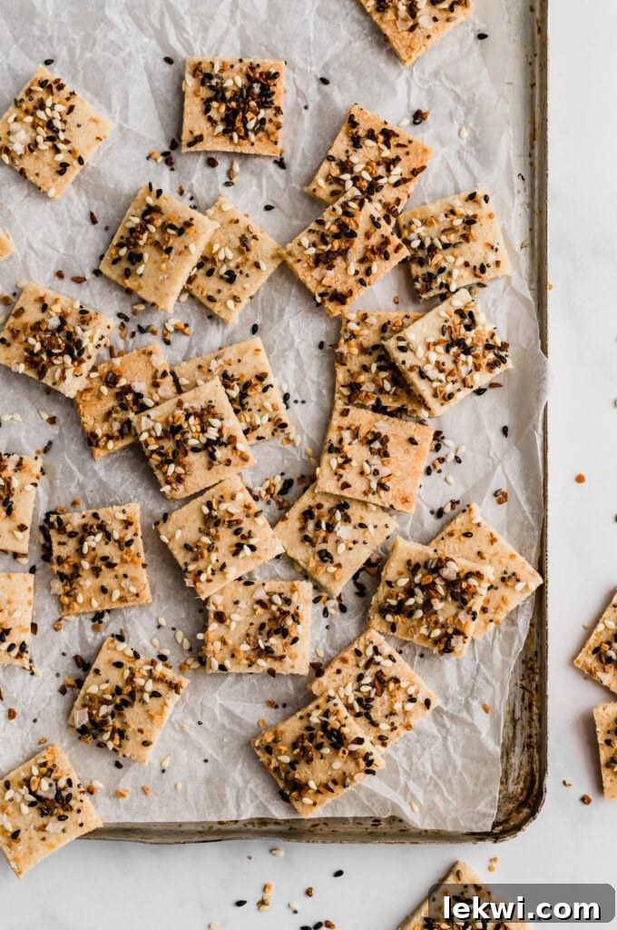 paleo everything bagel crackers stacked on a small board with a bowl of dip, highlighting their golden brown color and crunchy texture