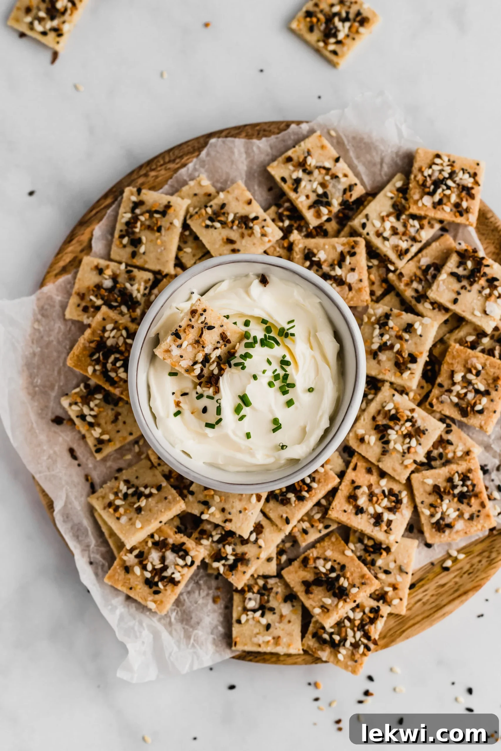 A platter filled with everything bagel crackers with a bowl of dip in the middle.
