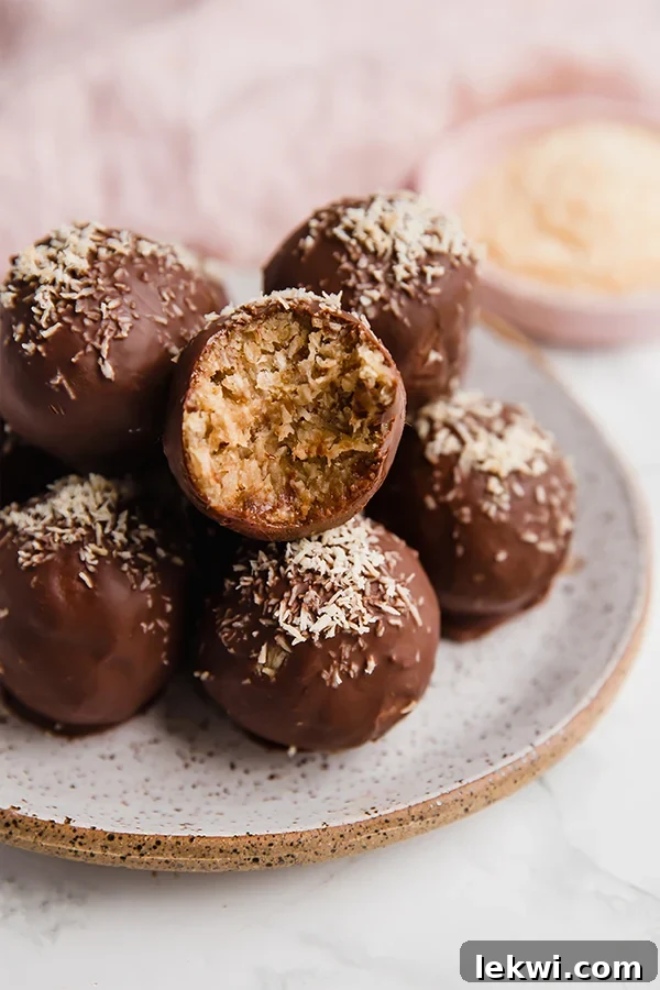 Chocolate covered samoa truffles on a small plate topped off with lightly toasted coconut, with a bite being taken out of one to show the soft coconut interior. 