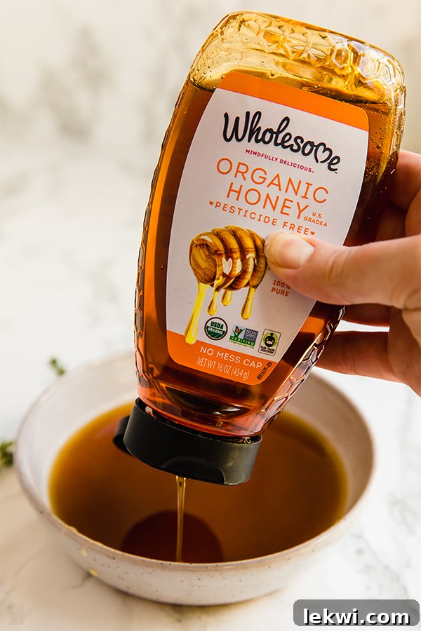 A hand squeezing organic honey into a bowl.