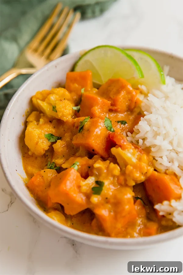 A white bowl filled with cauliflower rice and sweet potato cauliflower curry and fresh lime slices.