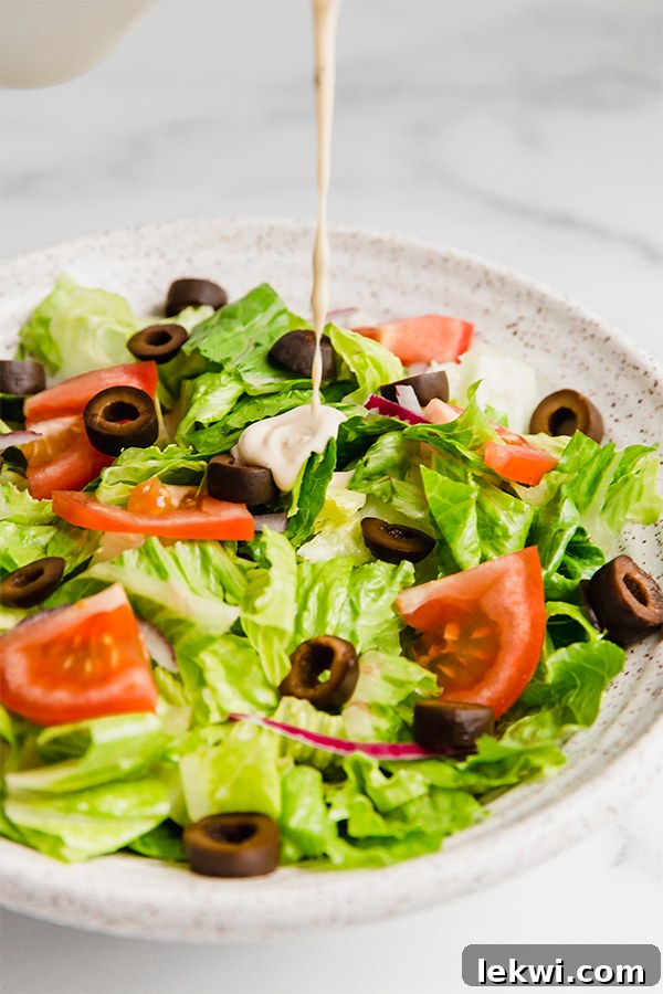 Creamy homemade Olive Garden copycat dressing in a clear glass container, with a wooden spoon, ready to be used on a fresh salad.