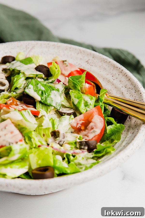 Freshly made Olive Garden copycat salad dressing in a small glass jar, garnished with a sprig of fresh basil, emphasizing its homemade quality.