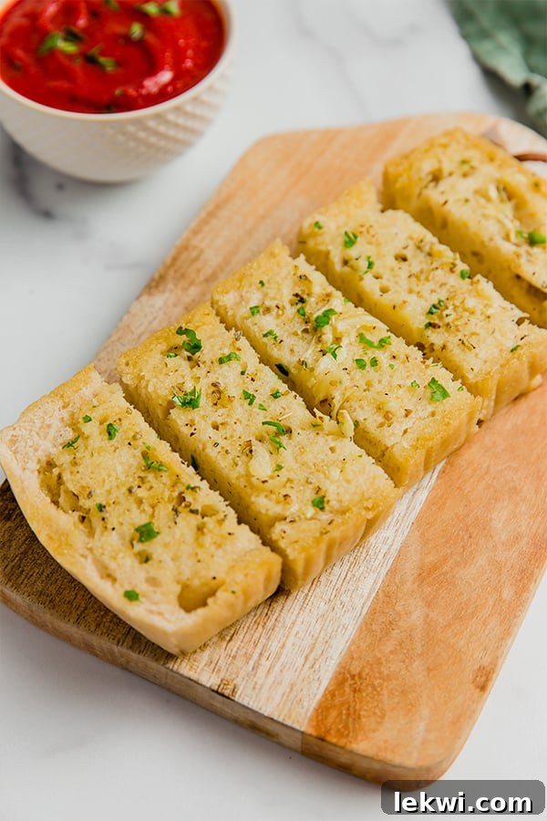 A loaf of gluten-free sourdough topped with garlic to make garlic bread cut into slices and on a wooden cutting board.