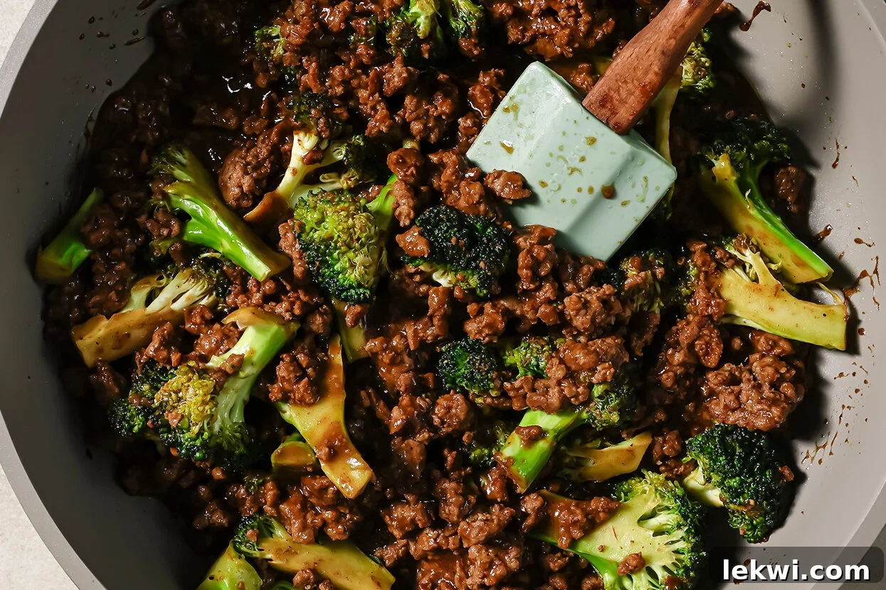 Ground beef and broccoli cooking in a pan with sauce.
