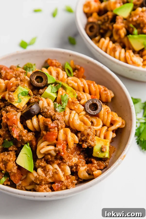 A white bowl filled with steaming, vibrant paleo taco pasta, garnished with fresh cilantro and avocado slices.