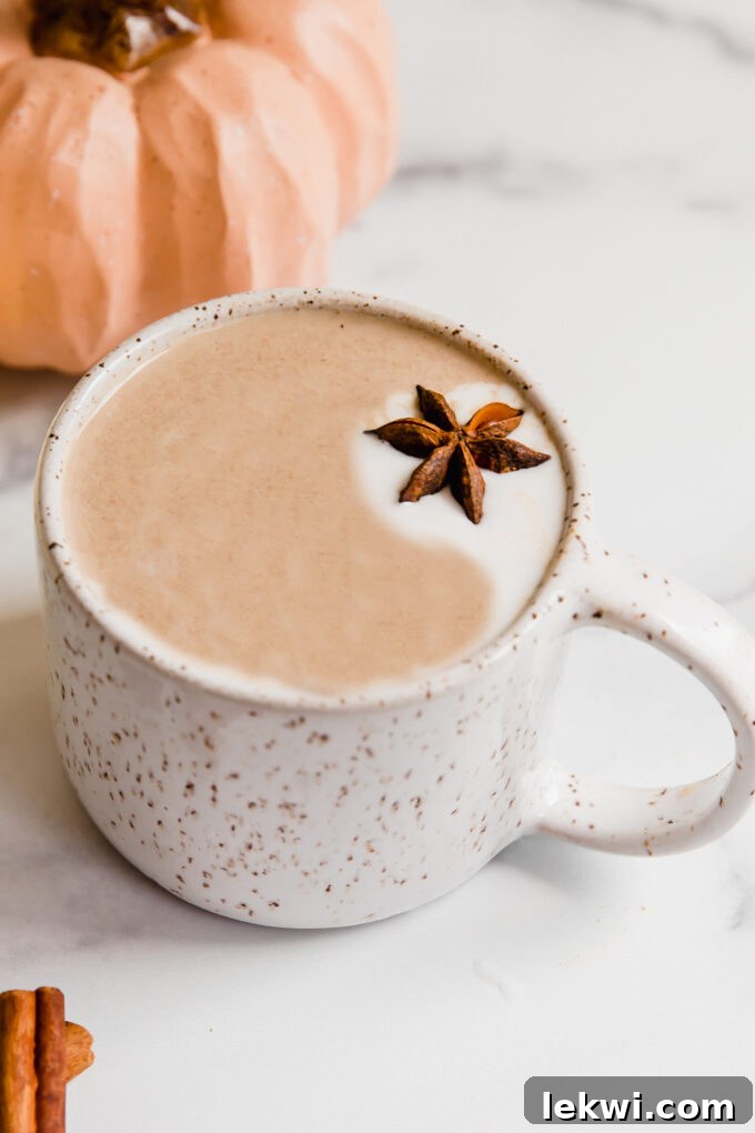 A warm Chai Pumpkin Spice Latte in a rustic mug, with autumn pumpkins in the soft-focus background, evoking fall coziness.