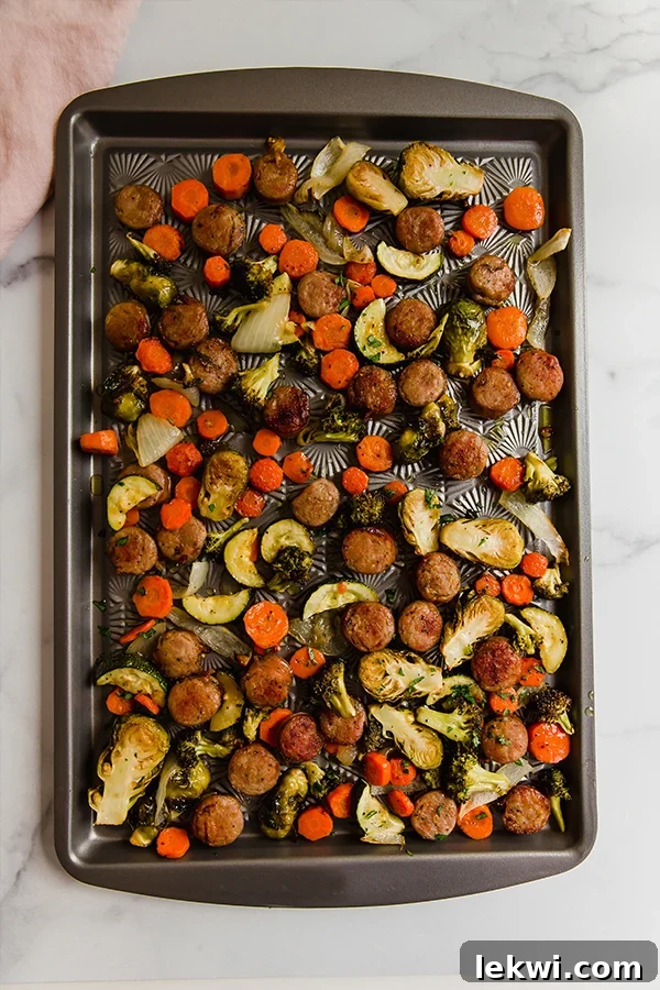 Close-up of roasted sausage and vegetables on a sheet pan, showing crispy edges.