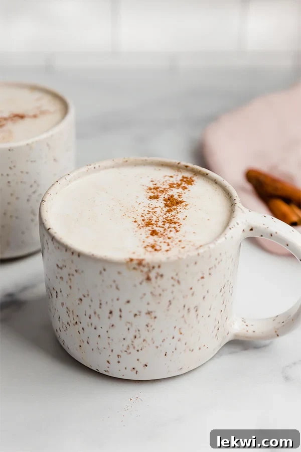A white ceramic mug filled with a snickerdoodle latte, topped with a dusting of cinnamon and ready to drink.