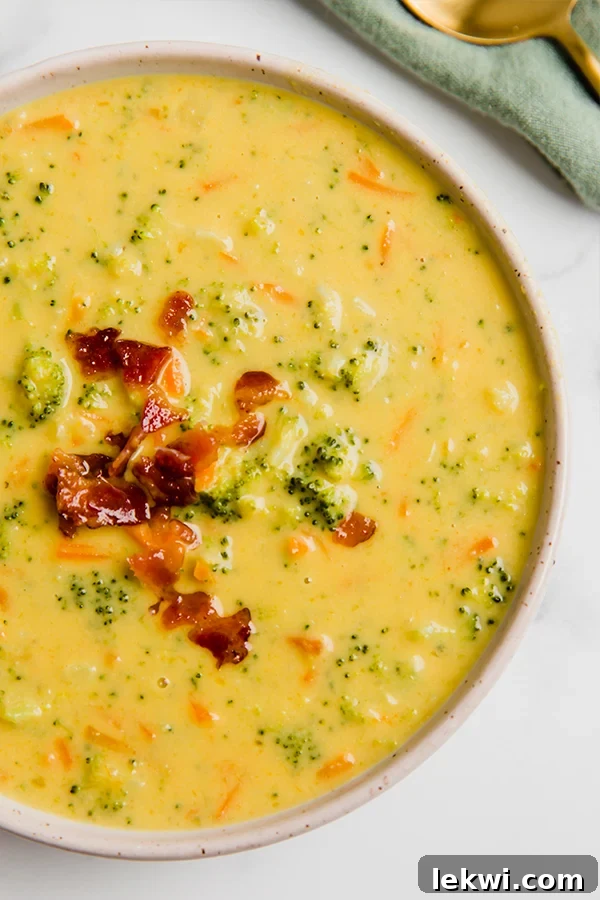 A white bowl filled with creamy, vibrant green dairy-free broccoli cheese soup, garnished with fresh herbs.