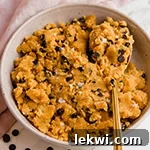 A white bowl filled with edible pumpkin chocolate chip cookie dough with a spoon in it.