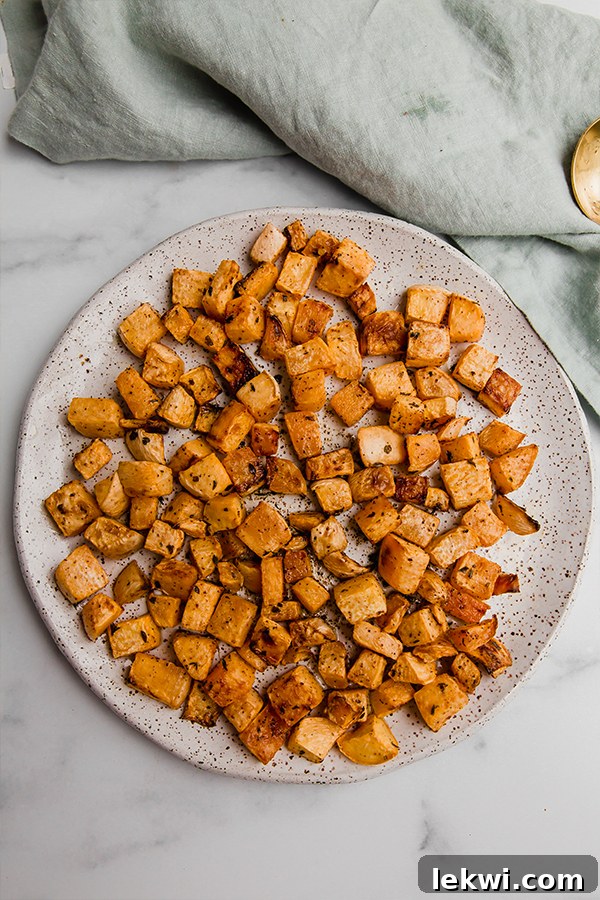 Three individual servings of oven roasted rutabaga on white plates, garnished, beautifully arranged and ready to be enjoyed.