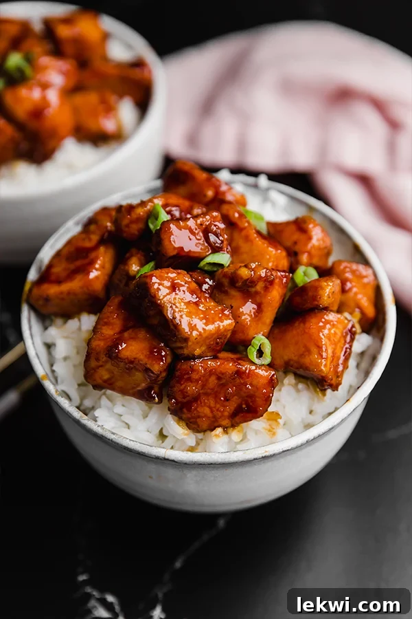 A white bowl filled with cauliflower rice topped with paleo general tso\'s chicken.