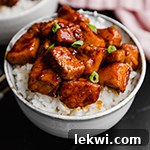 A white bowl with cauliflower rice topped with paleo general tso's chicken.