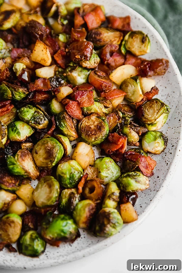 A beautifully speckled plate overflowing with the rich, caramelized Bacon, Date & Apple Brussels Sprout Skillet, showcasing crispy bacon, tender Brussels sprouts, soft apples, and chewy dates.