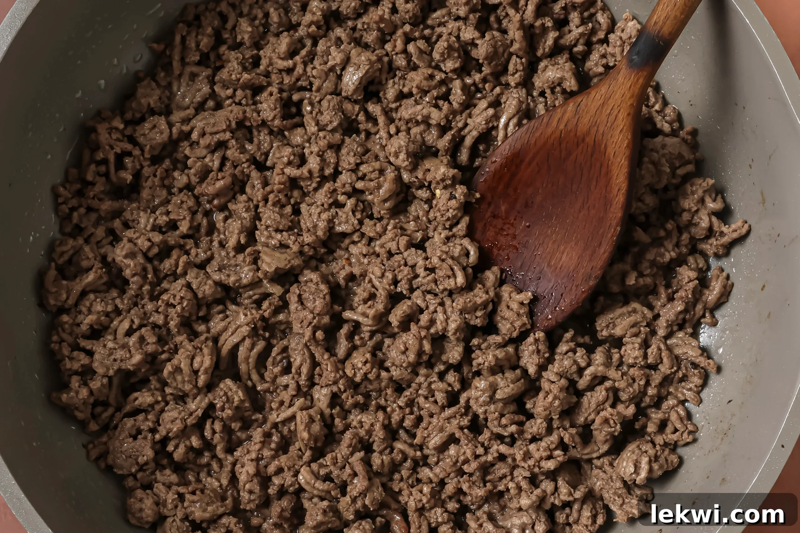 A wooden spoon browning ground beef in a large skillet.