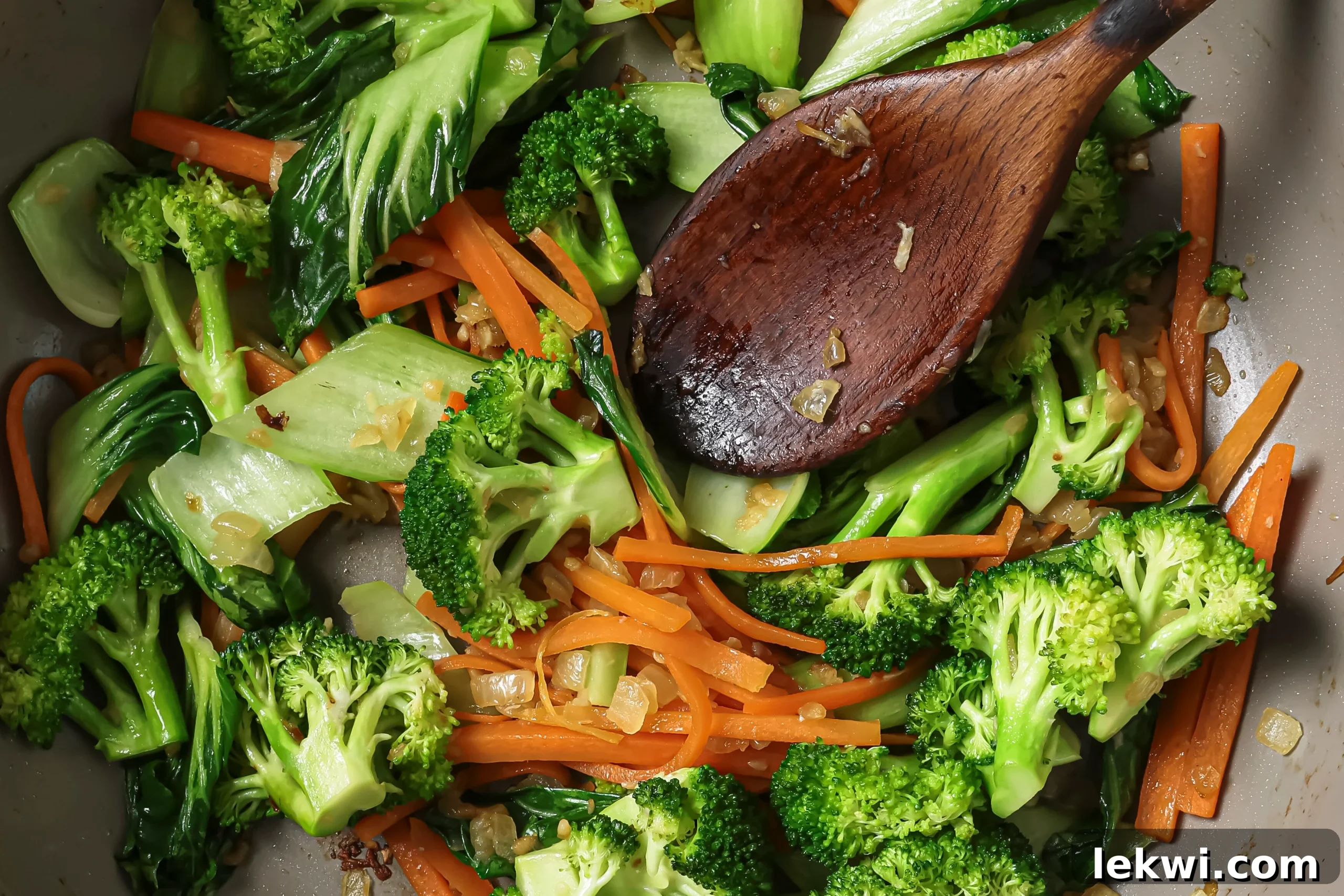 A wooden spoon sautéing diced onions and minced garlic in a pan.