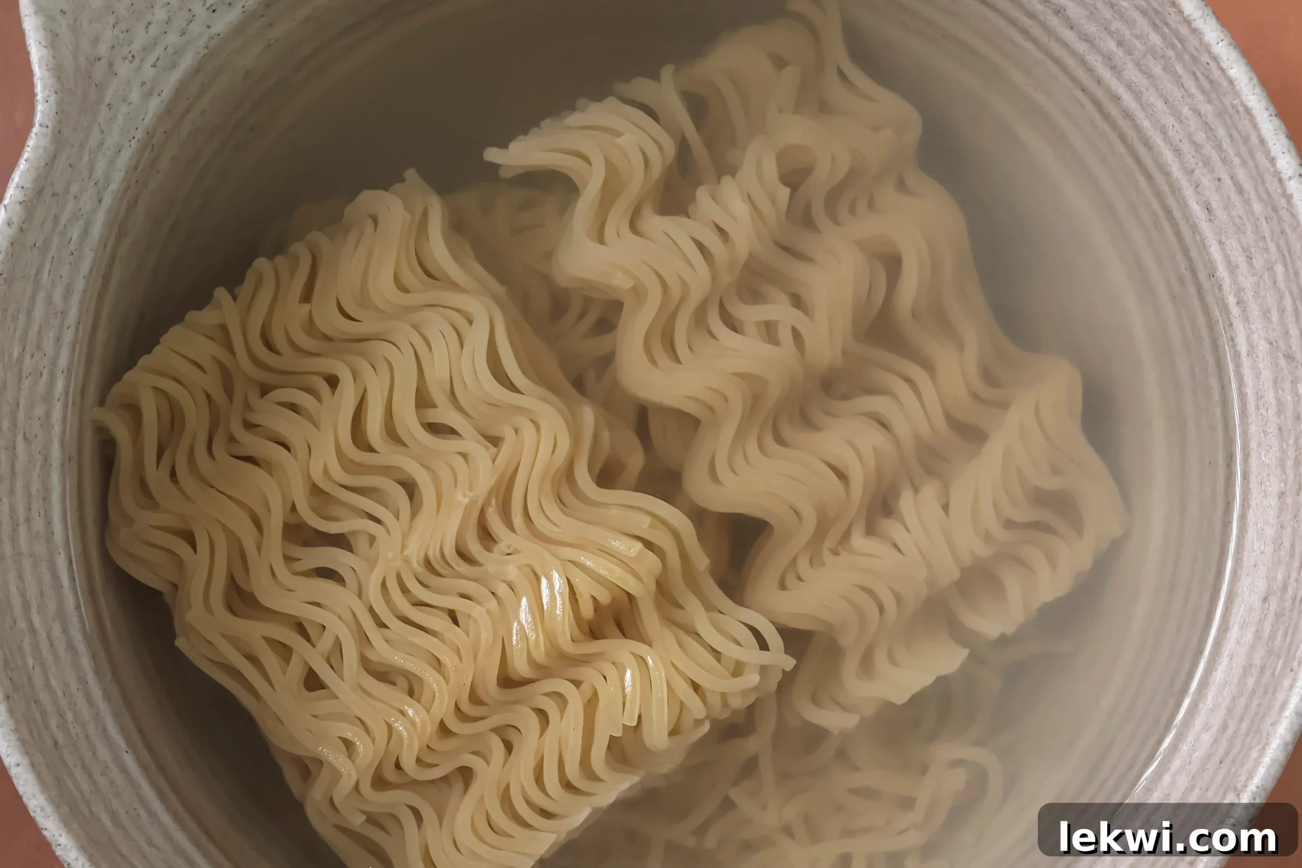 A bowl of hot water softening a block of ramen noodles.