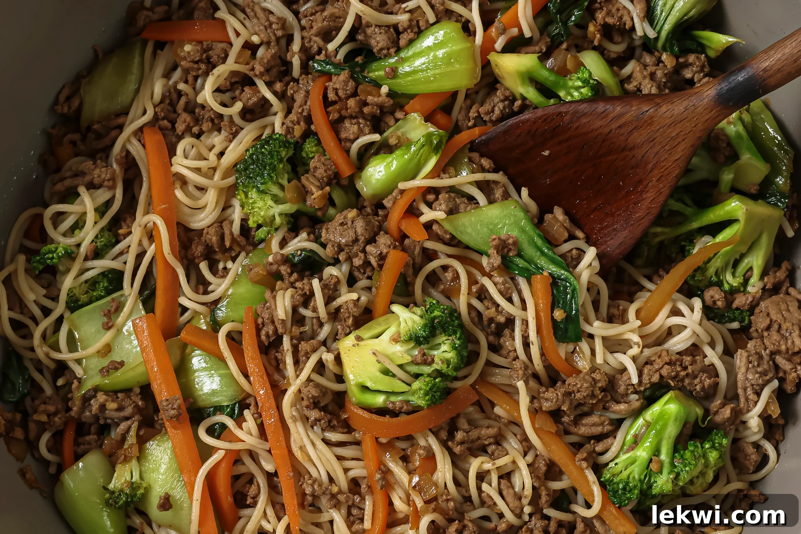 The beef, vegetables, and ramen noodles sautéing together in a large pan, coated in sauce.