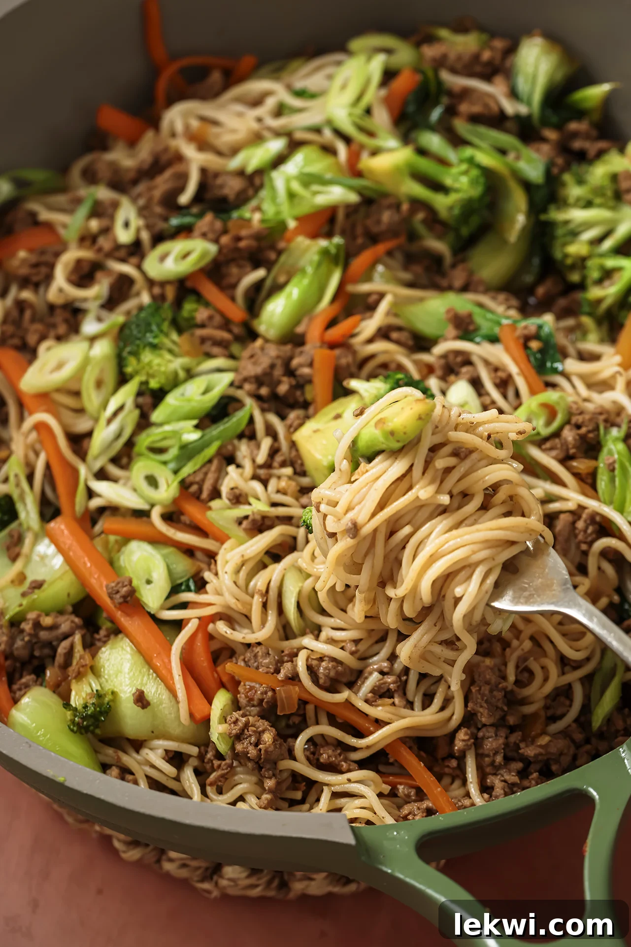 A fork digging into a pan of ground beef ramen noodle stir fry, showcasing the delicious blend of ingredients.