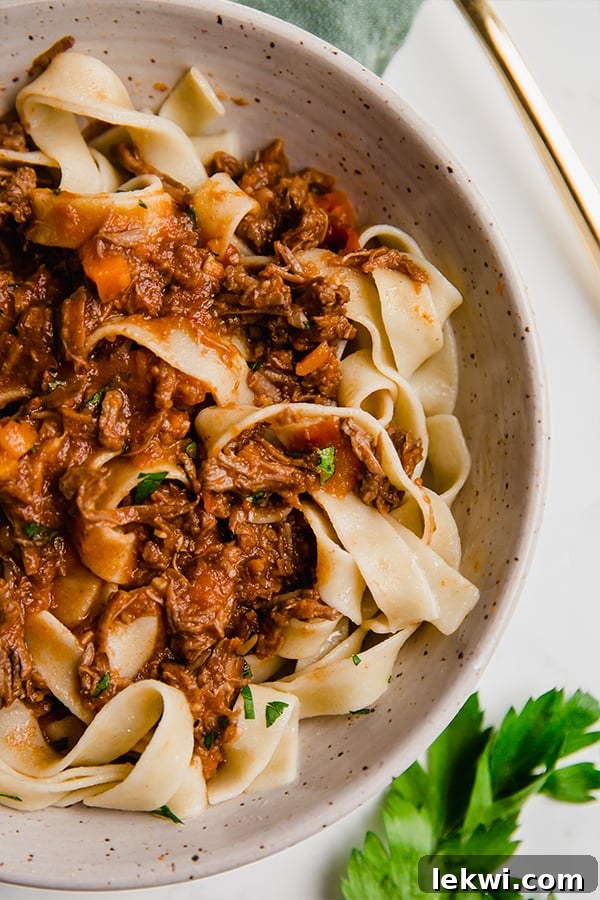 A white bowl filled with slow cooker beef ragu over pasta.