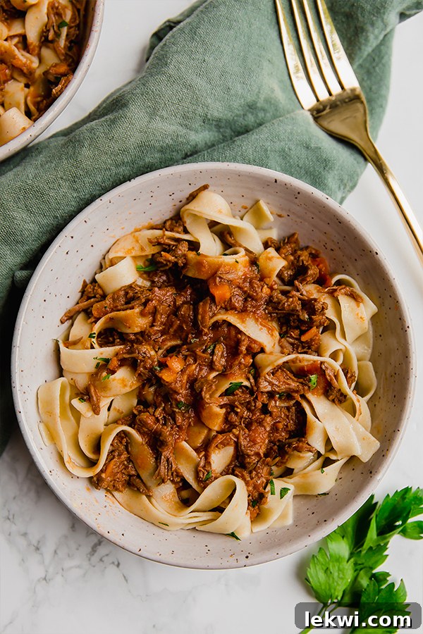 beef ragu in two bowls with green cloth and gold fork