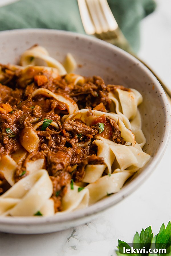A white bowl filled with slow cooker beef ragu over pasta.