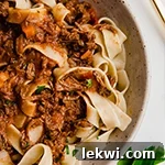A white bowl filled with slow cooker beef ragu over pasta.