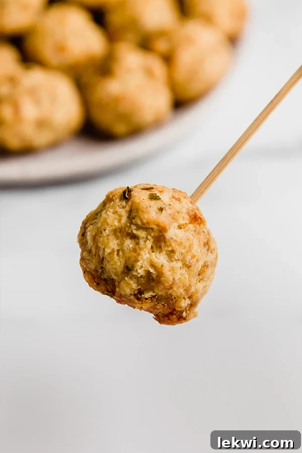 A close-up view of a single, perfectly golden-brown paleo sausage ball, speared with a toothpick, inviting a bite.