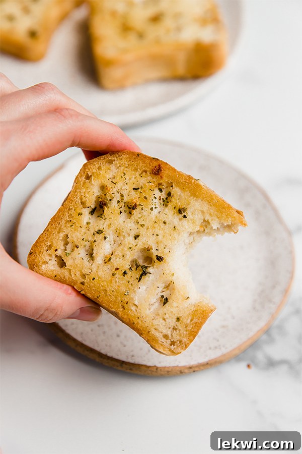 A hand holding a piece of gluten-free Texas toast with a bite taken out, showing the crispy texture.