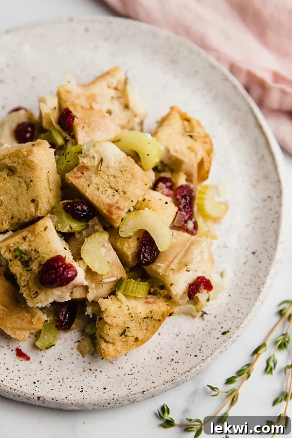 A perfectly portioned serving of golden gluten-free stuffing, garnished with fresh rosemary, presented on a white plate.