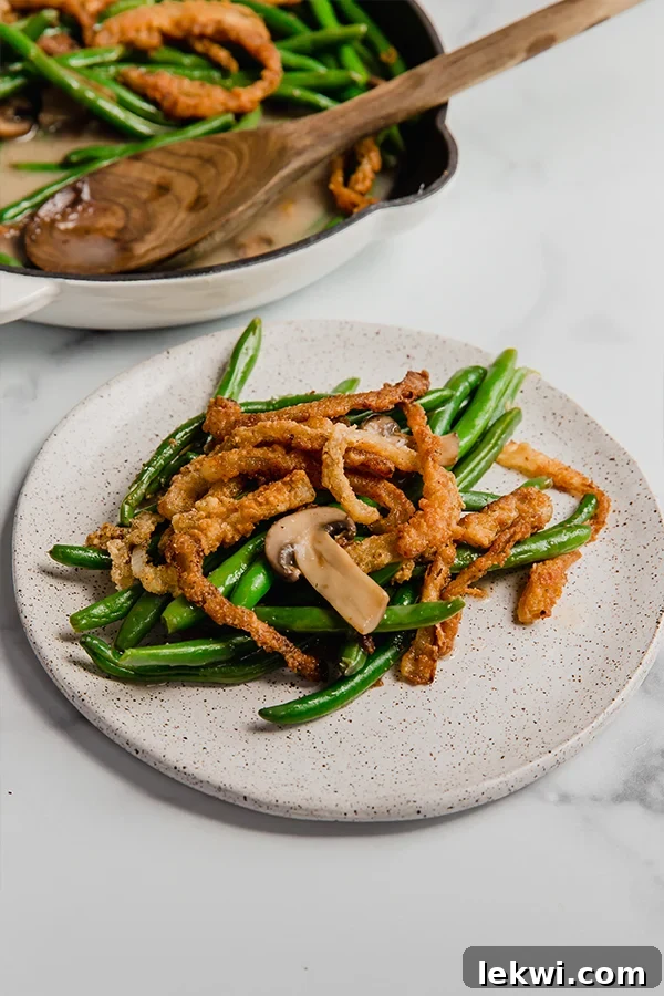 Green Bean Casserole in a Skillet and a serving on a plate, adorned with golden fried onions.