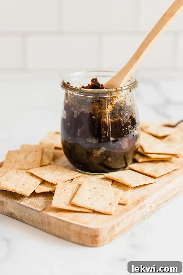 A glass jar brimming with homemade apple bacon jam, presented alongside a collection of crispy crackers, highlighting its perfect texture and appetizing appeal.