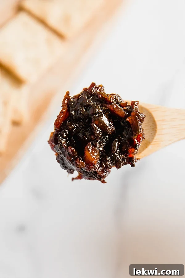 A wooden spoon delicately scooping a portion of homemade apple bacon jam, showcasing its rich, chunky texture and inviting deep color.