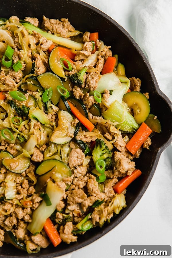 Ground turkey and veggie stir fry topped with green onion in a black pan.
