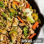 Ground turkey and veggie stir fry topped with green onion in a black pan.
