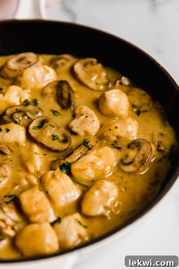 Serving of creamy chicken stroganoff with fresh parsley, served in a bowl with mashed sweet potato.