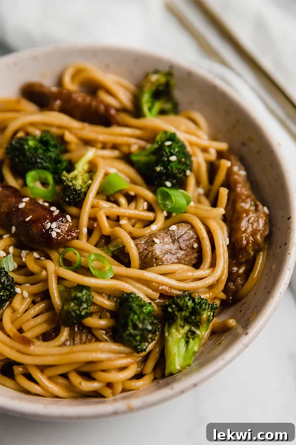 Delicious Gluten-Free Beef and Broccoli Lo Mein, garnished with fresh green onions and sesame seeds, served in a large pan.