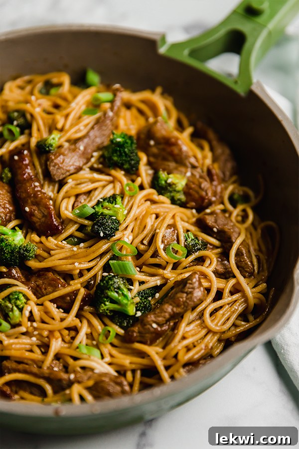 A close-up shot of a single pan filled with steaming gluten-free beef and broccoli lo mein.