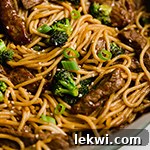 Gluten free and broccoli lo mein topped with green onions and sesame seeds in a pan topepd with sesame seeds.